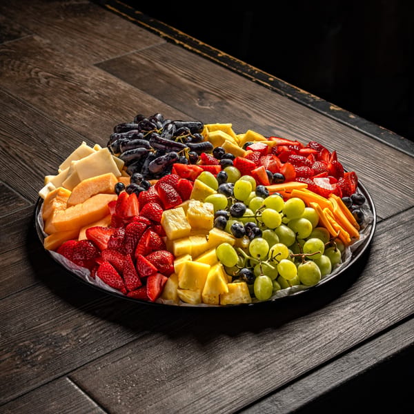A large platter of fresh fruit and cheese on a dark wooden table.