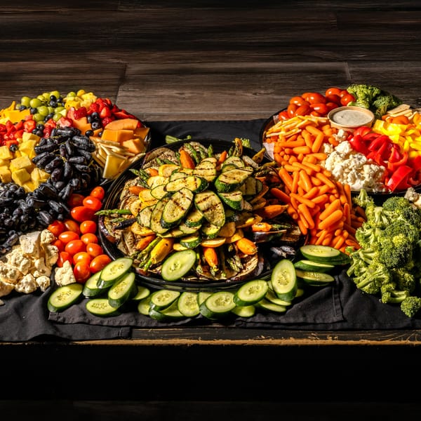 Three large platters overflowing with fresh fruits, grilled vegetables, and raw vegetables with dip.