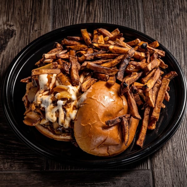 A black plate holds a burger with caramelized onions and white sauce, alongside a pile of fries.